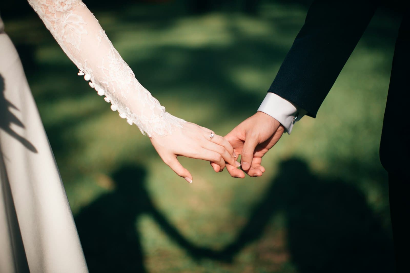 Couple holding hands with shadows on sunlit grass
